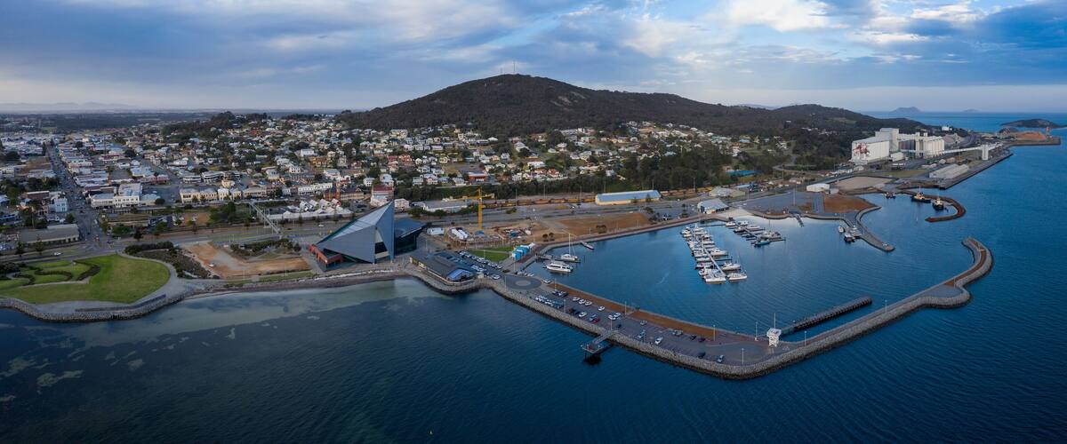 An aerial view of a coastal town with a marina, residential area, and a large industrial building.