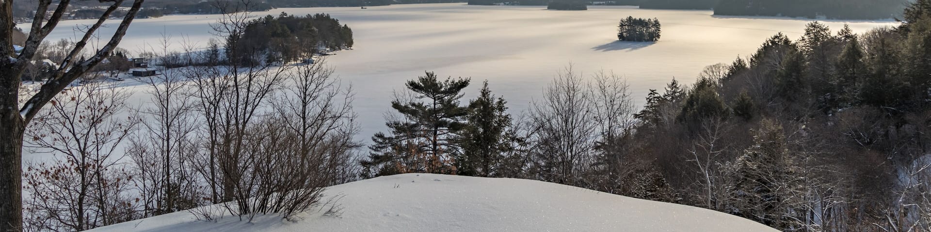 A snow-covered landscape with a lake, trees, and a clear sky.