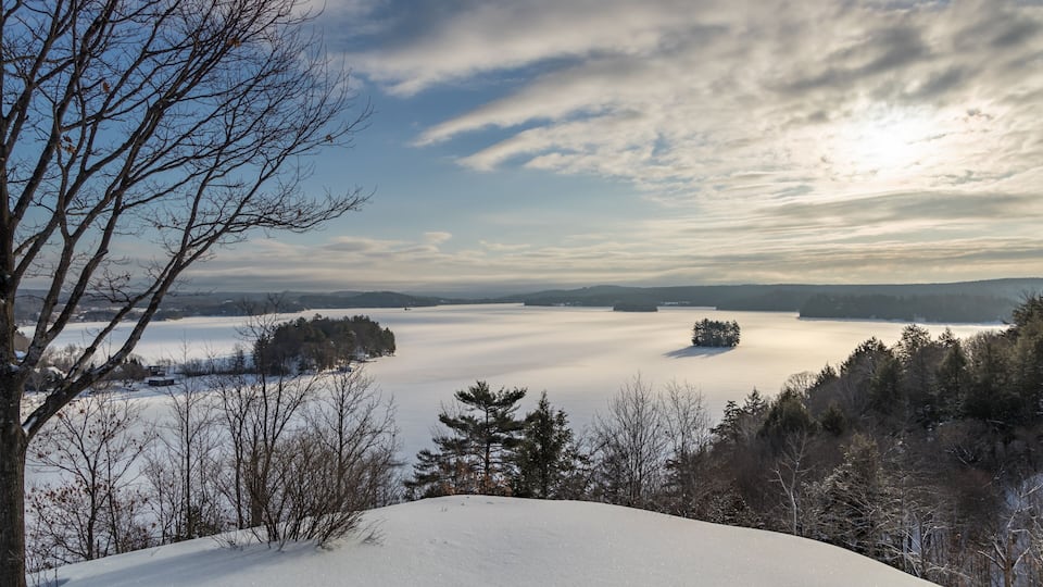 A snow-covered landscape with a lake, trees, and a clear sky.