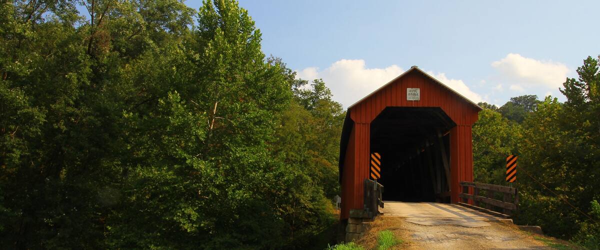 A red covered bridge with a sign, surrounded by lush greenery and trees.