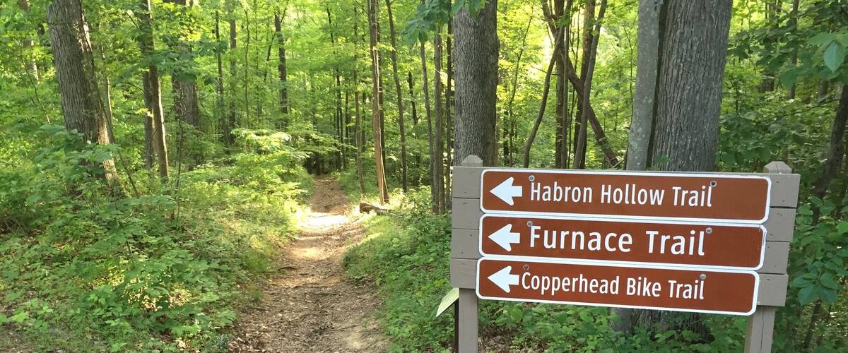 A trail sign in a forest with paths to Habron Hollow Trail, Furnace Trail, and Copperhead Bike Trail.