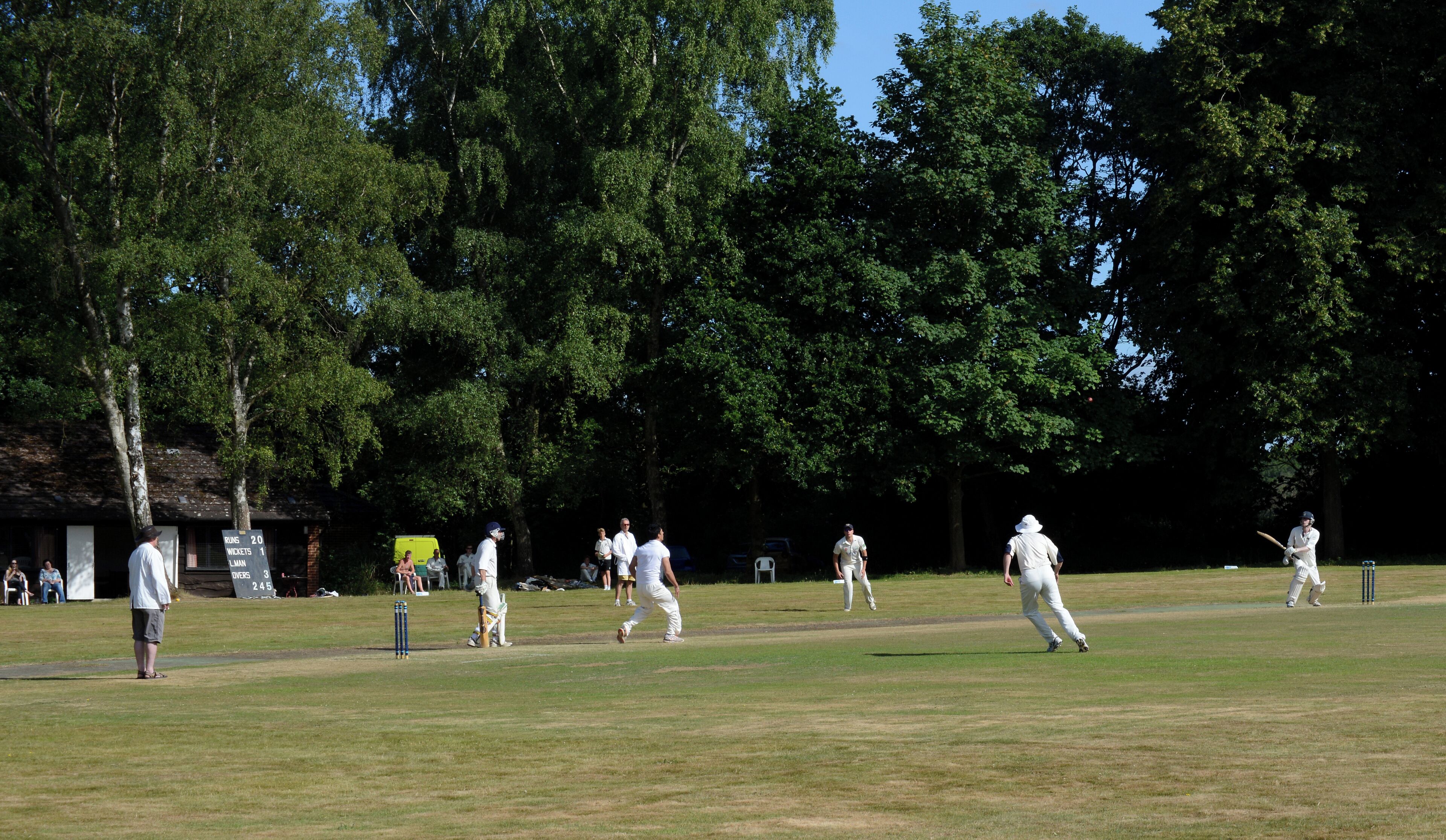 A cricket match in progress on a sunny day with players in white uniforms.