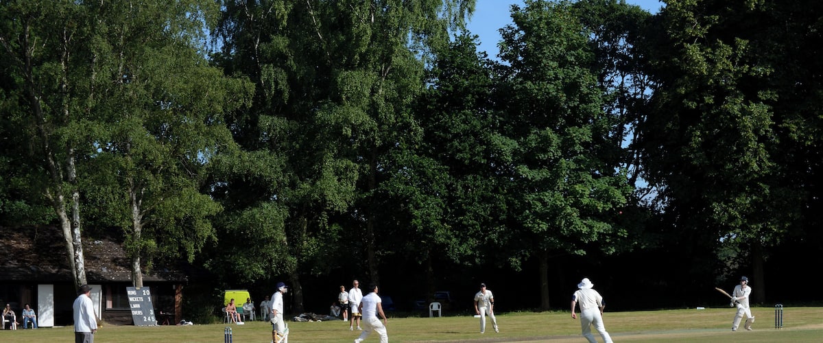 A cricket match in progress on a sunny day with players in white uniforms.