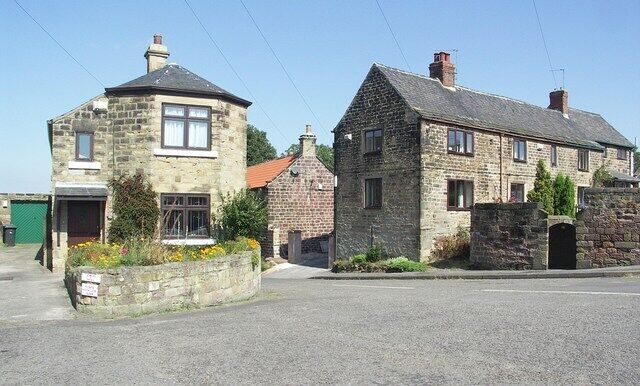 A stone house with a red roof, a stone wall, and a garden with flowers.