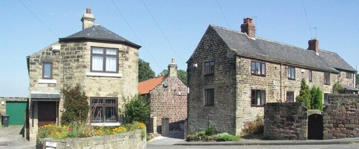 A stone house with a red roof, a stone wall, and a garden with flowers.