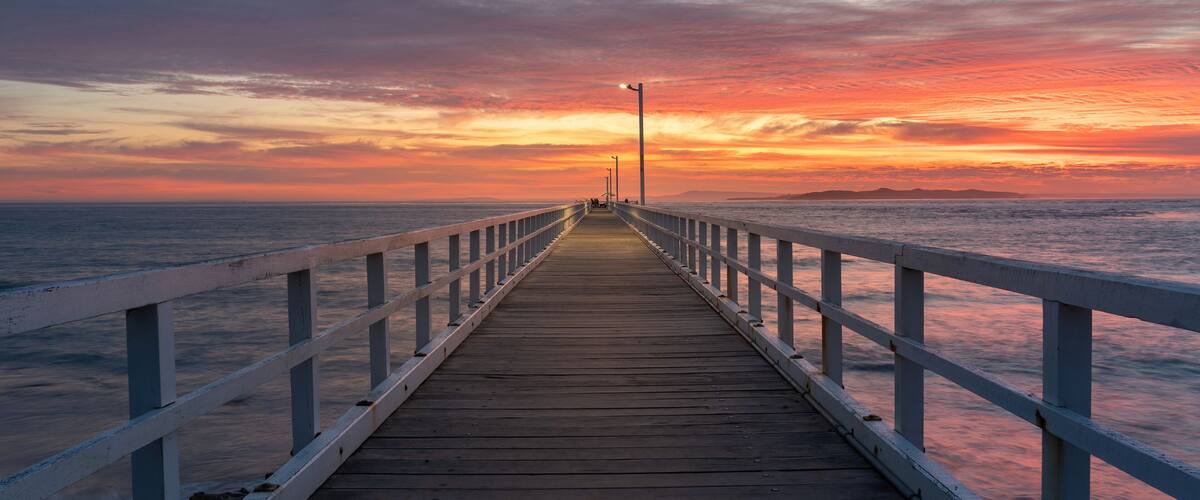 A wooden pier extending into the ocean at sunset with a colorful sky.