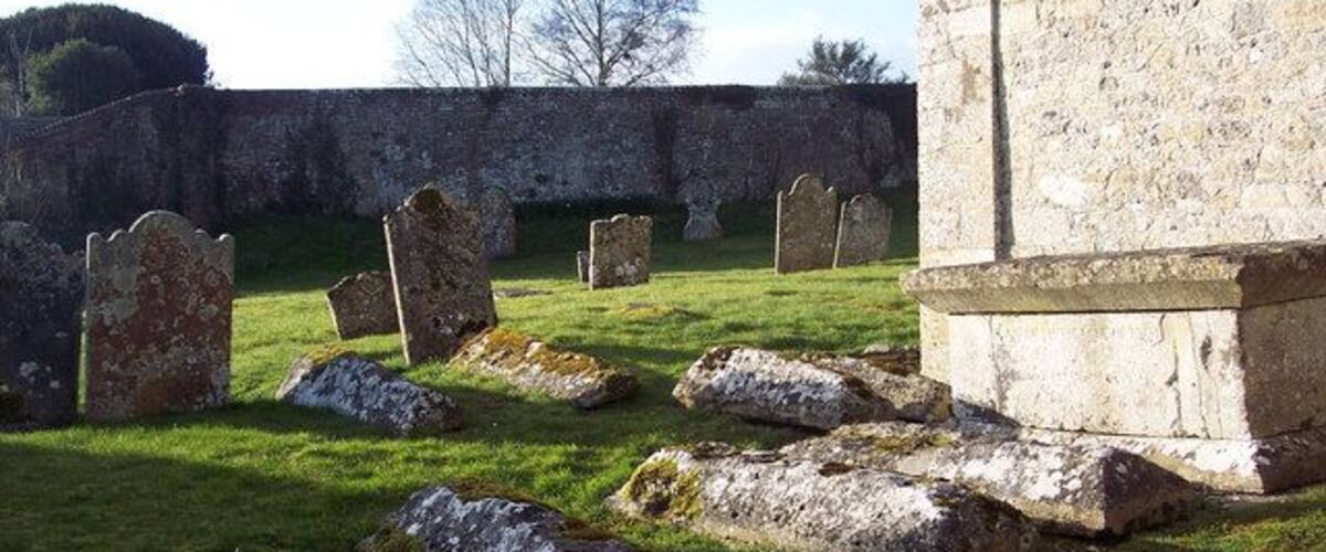 A cemetery with headstones and a stone wall.