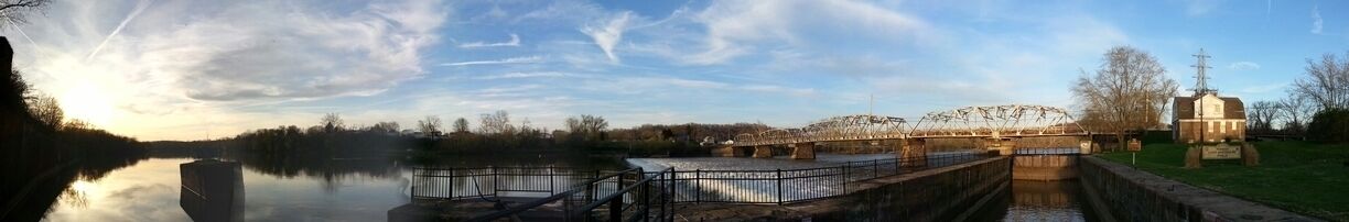A calm river with a bridge, a lock system, and a small building.