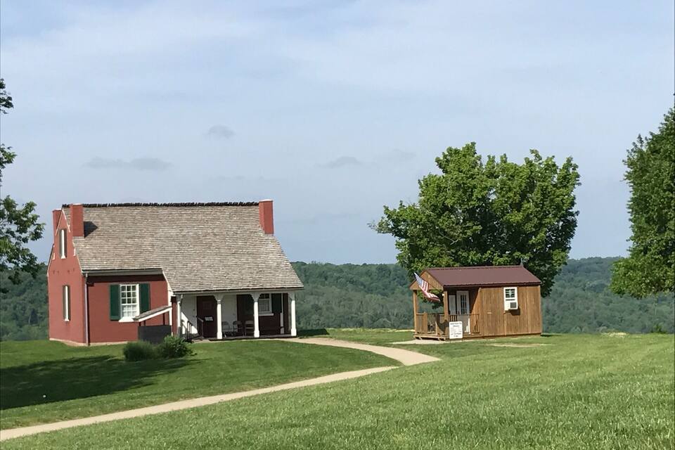 A red house with a porch and a small wooden structure with an American flag.