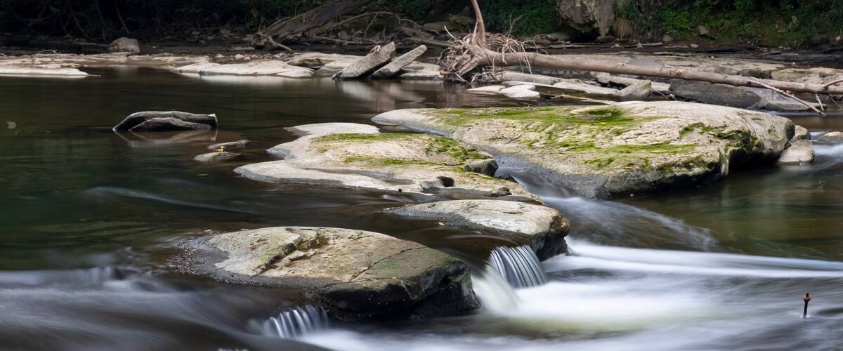 A river with a smooth water flow over rocks, surrounded by a forested area.