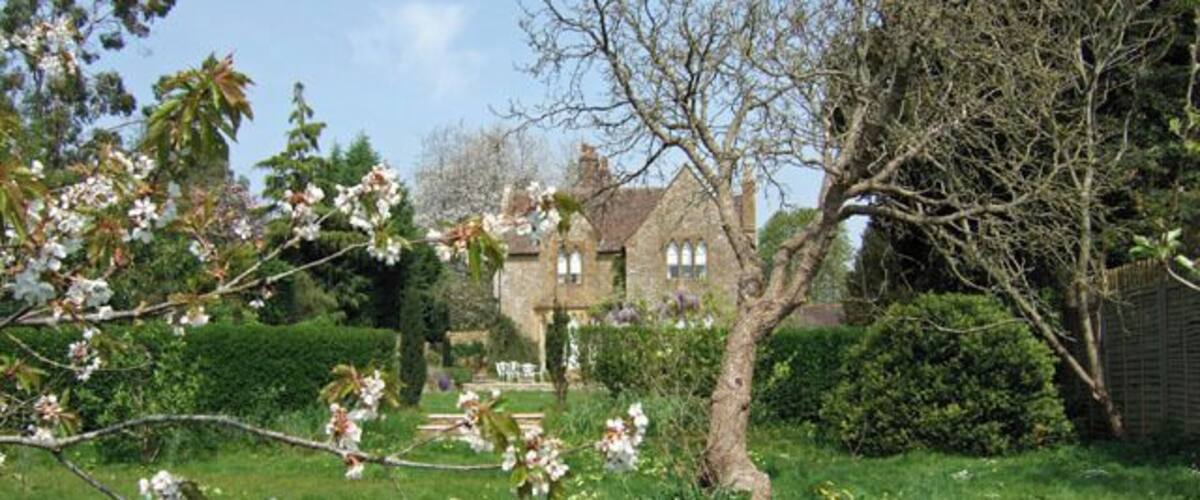 A garden with blooming trees, a lawn, and a stone building in the background.