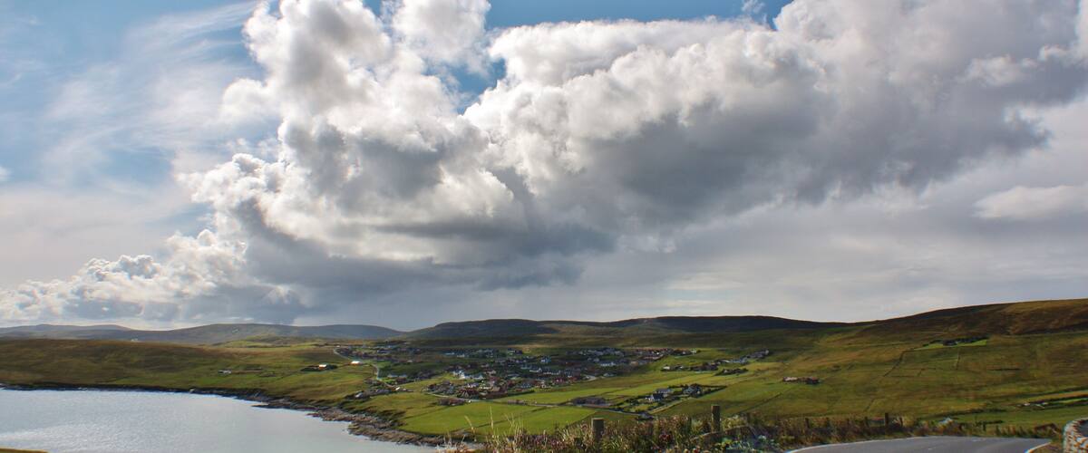 A coastal village with a lake, rolling hills, and a partly cloudy sky.