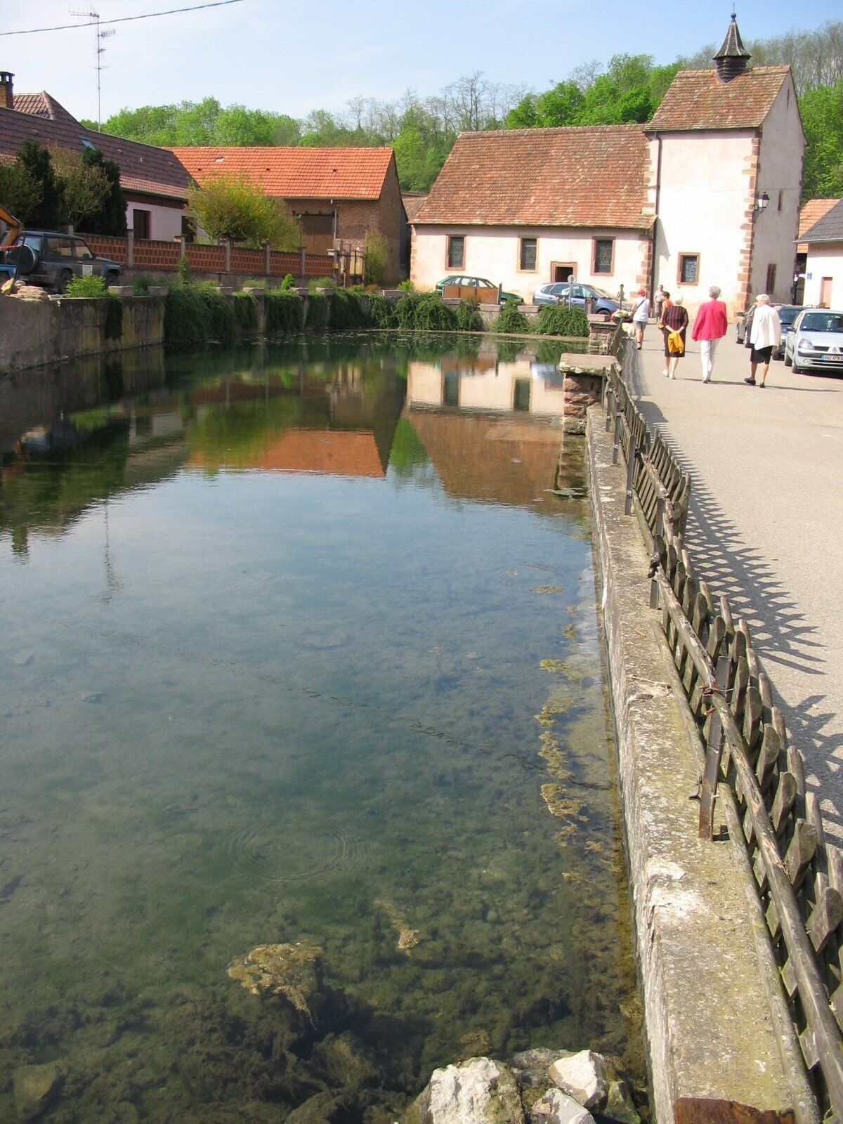 A clear water body with a wooden railing, surrounded by traditional buildings with red-tiled roofs.