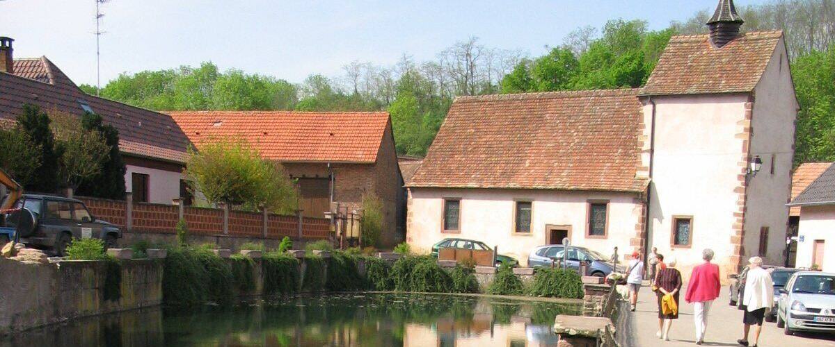 A clear water body with a wooden railing, surrounded by traditional buildings with red-tiled roofs.