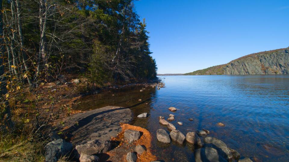 A clear lake with rocky shores, surrounded by dense forest and a distant mountain.