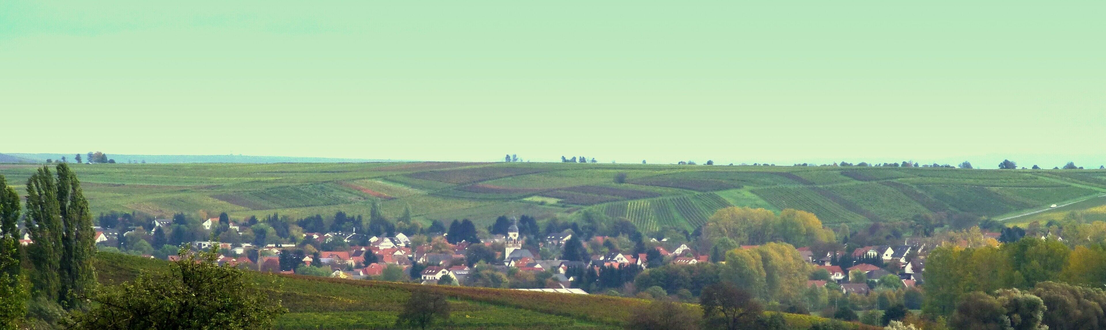 A rural landscape with rolling hills, a village with red-roofed houses, and a church tower.