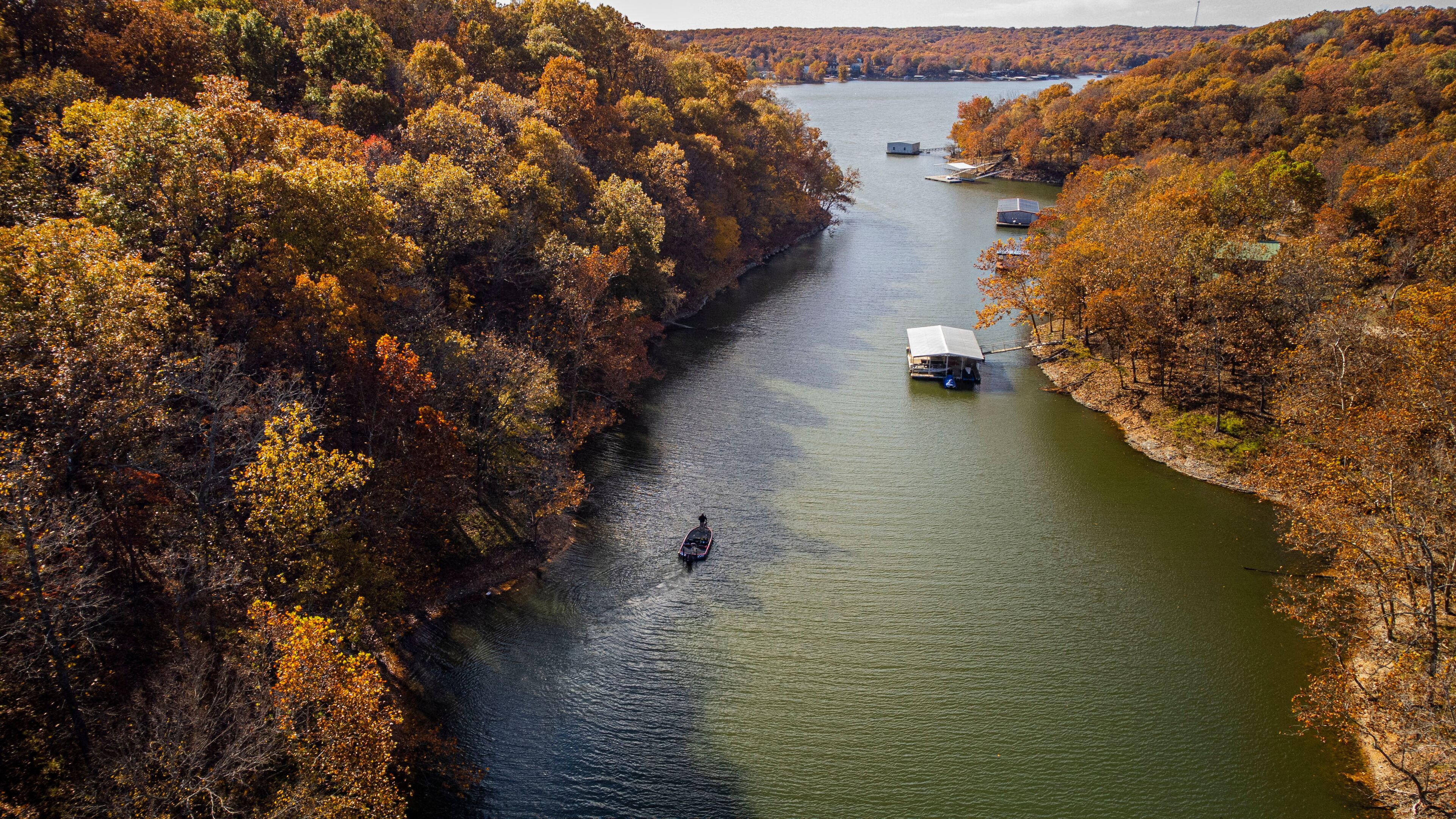 A river surrounded by autumn-colored trees, a boat, and a small dock with a house.