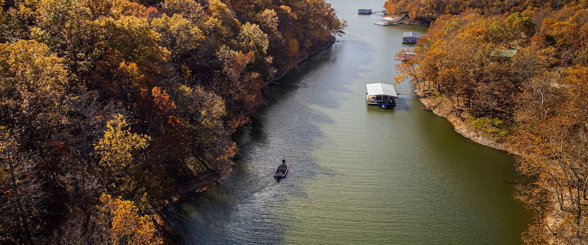 A river surrounded by autumn-colored trees, a boat, and a small dock with a house.