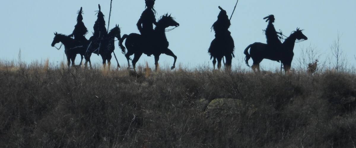 Silhouettes of people on horseback in a grassy field.
