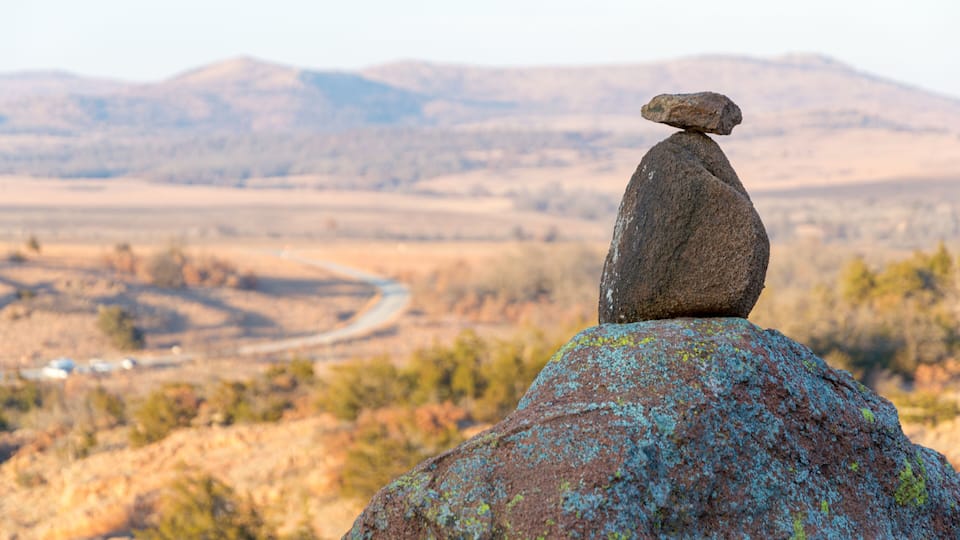 A balanced rock formation on a large rock with a valley and mountains in the background.