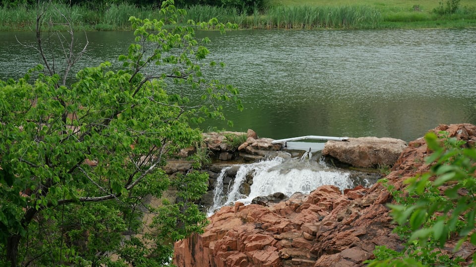 A waterfall cascading over red rocks into a calm lake surrounded by lush greenery.
