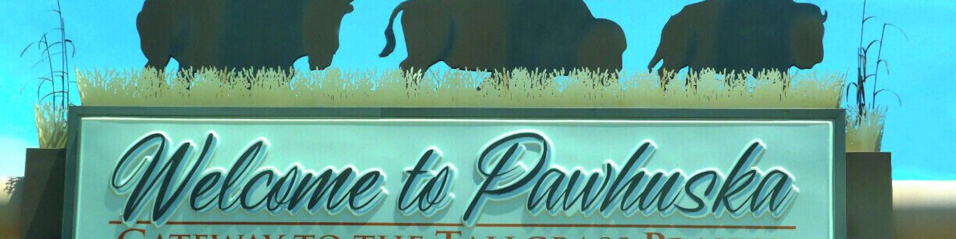 Un cartel con siluetas de bisontes y el texto: 'Bienvenidos a Pawhuska, puerta de entrada a la pradera de hierba alta.'