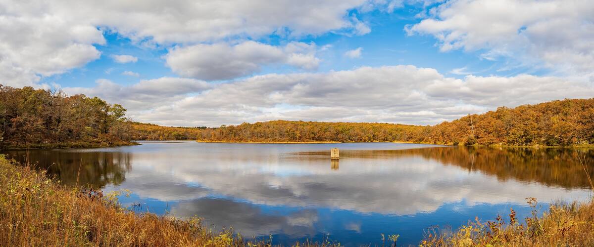 A calm lake surrounded by autumn-colored trees and a clear sky.