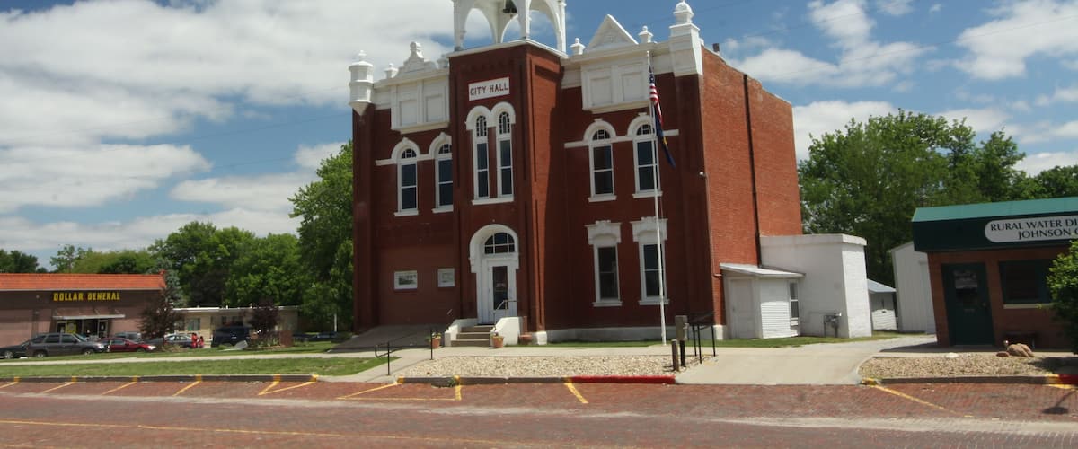 A historic red brick building with a white tower and clock, surrounded by a parking lot and greenery.