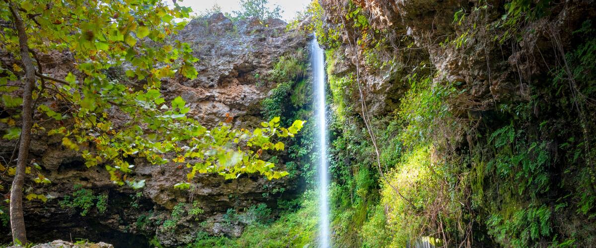 A waterfall cascading into a pool surrounded by lush greenery and rocky cliffs.