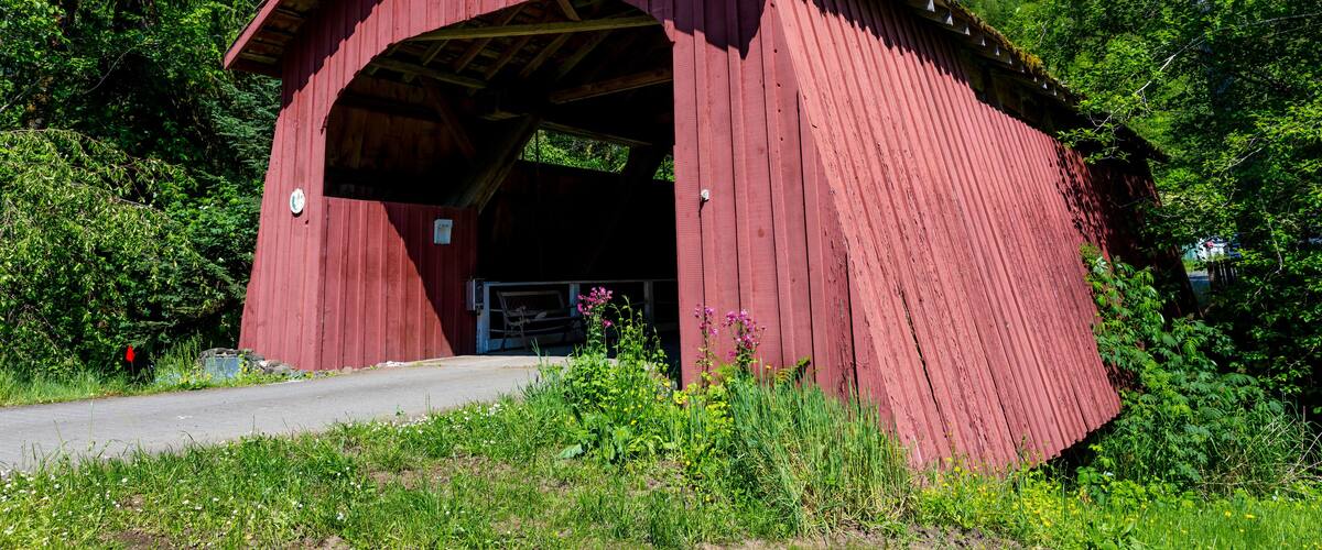 A red covered bridge with a sign reading "Dirt Creek 1914" in a forested area.