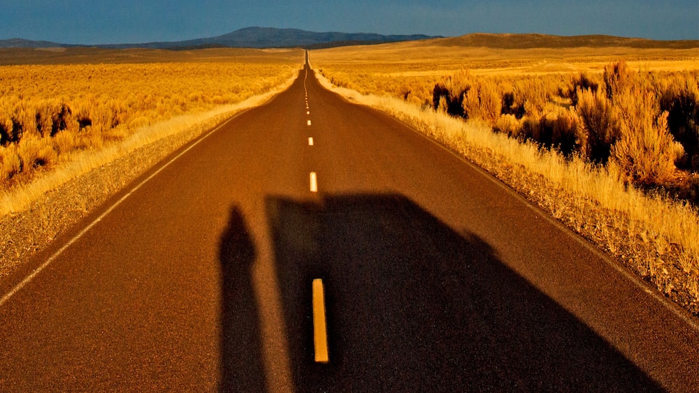 A straight road flanked by dry grasslands under a clear sky.