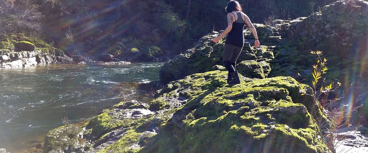 A person standing on a moss-covered rock by a river.