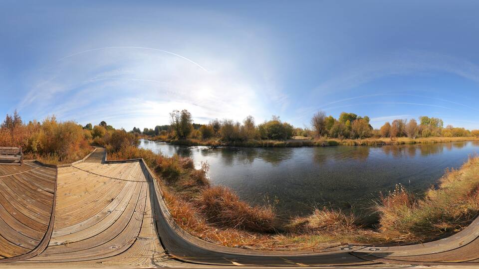 A wooden boardwalk curving around a calm lake with autumn foliage in the background.