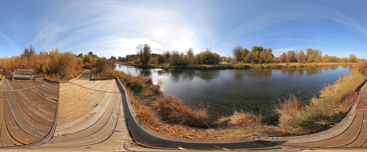 A wooden boardwalk curving around a calm lake with autumn foliage in the background.