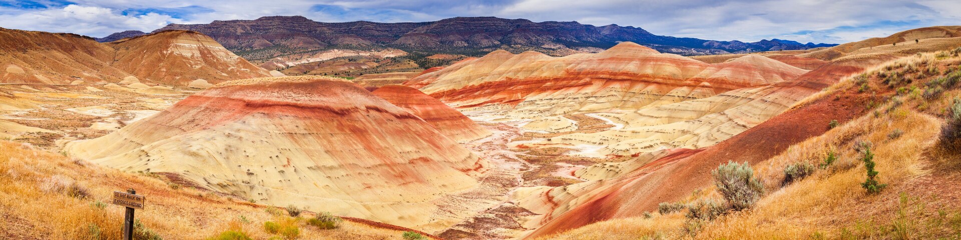 Paisagem colorida com colinas onduladas e uma placa de aviso.