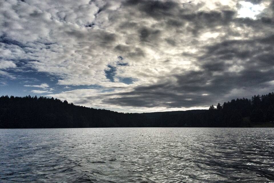 A lake with a forested shoreline and a cloudy sky.