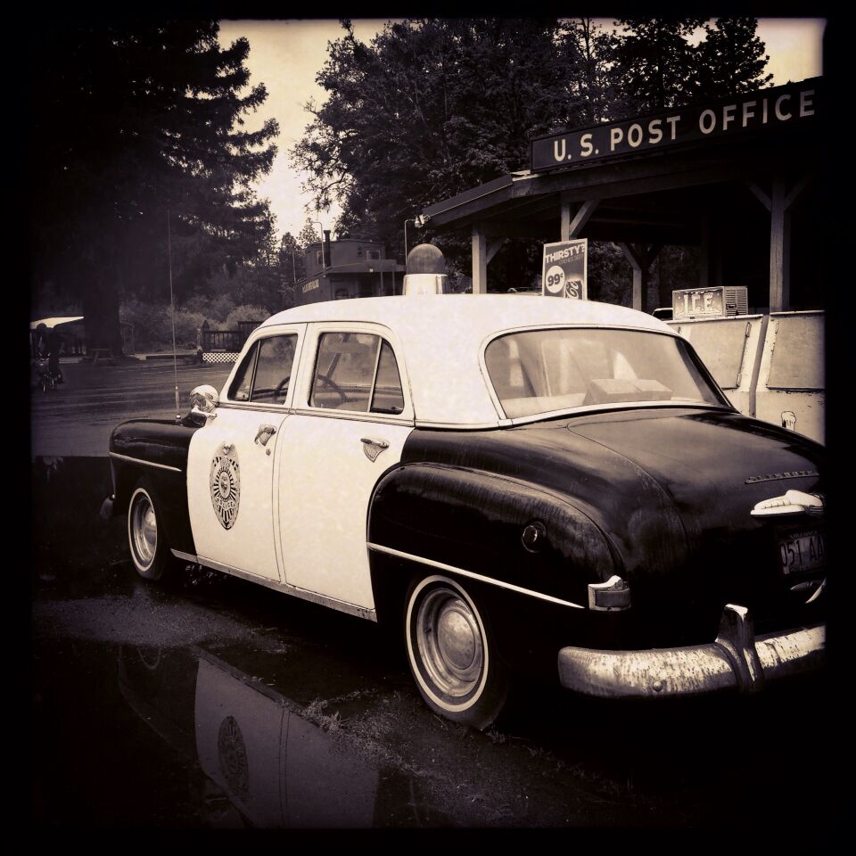 A vintage U.S. Post Office police car parked in front of the U.S. Post Office building.