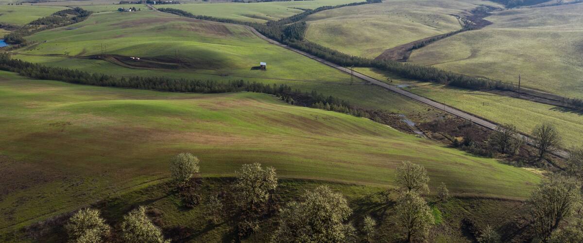 Rolling green hills, a winding road, and a small white building in a rural landscape.