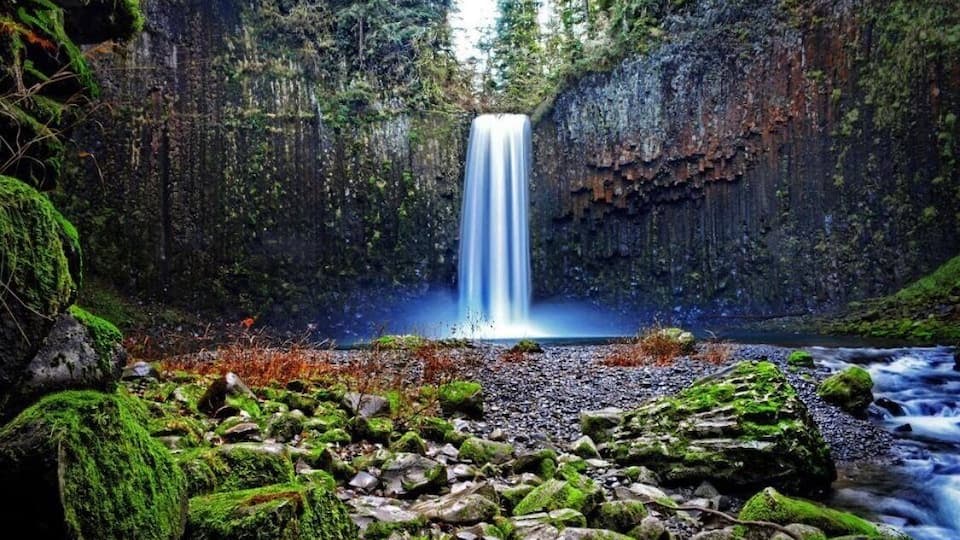 A waterfall cascading down a rocky cliff surrounded by moss-covered rocks and vegetation.
