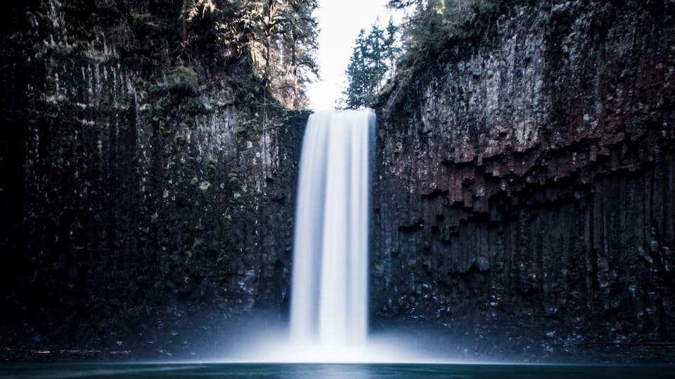 A waterfall cascading into a calm river surrounded by rocky cliffs.