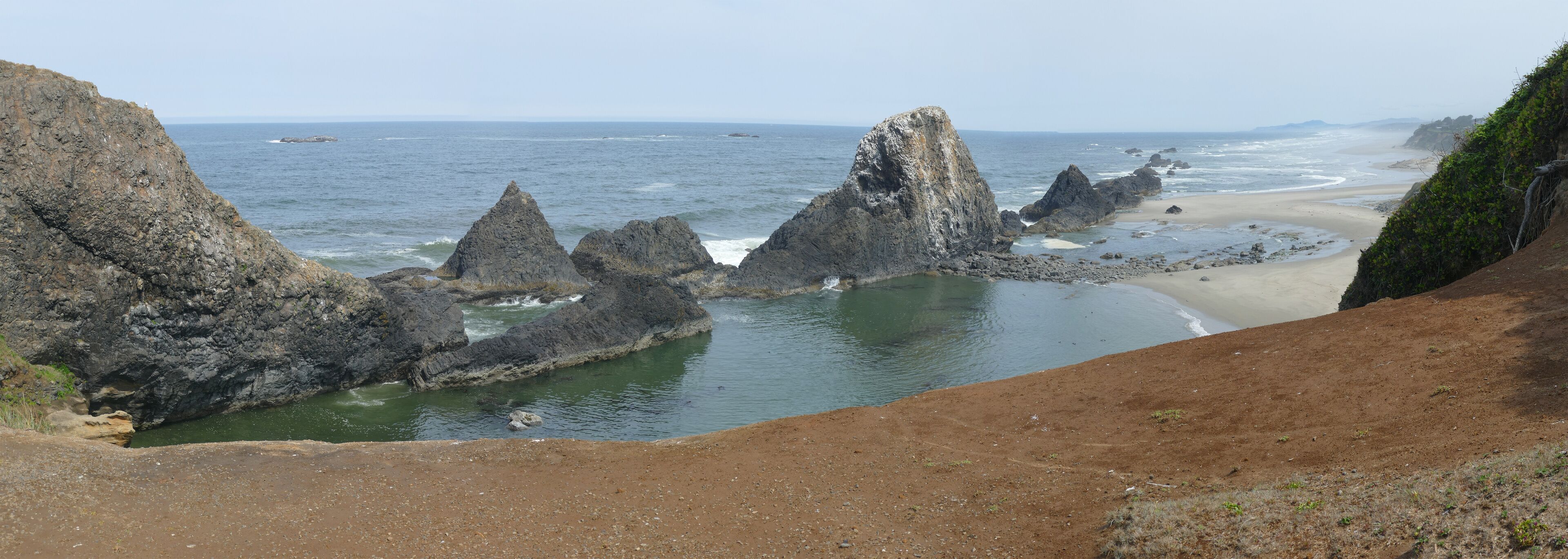 A coastal landscape with rocky formations, a sandy beach, and a clear view of the ocean.