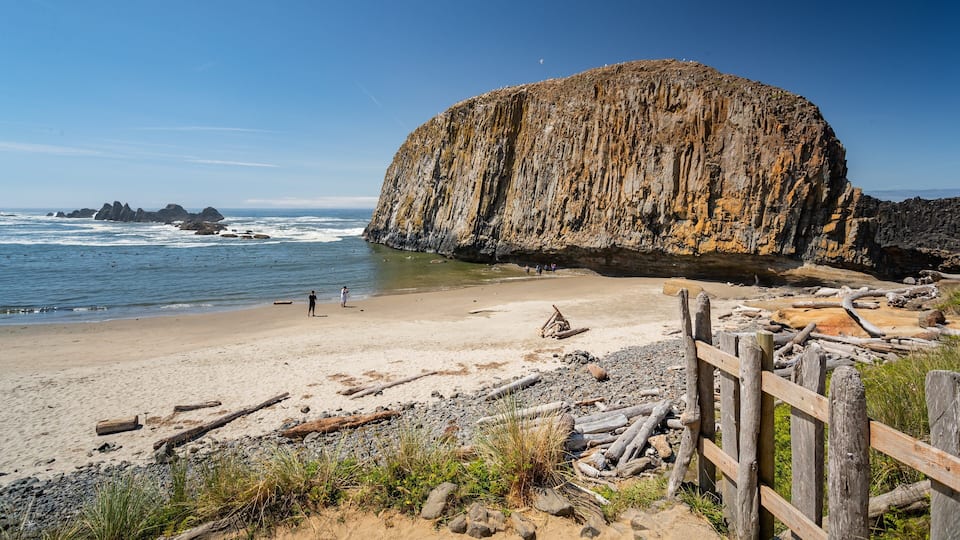 A rocky cliff by the sea, a sandy beach, and a wooden fence.