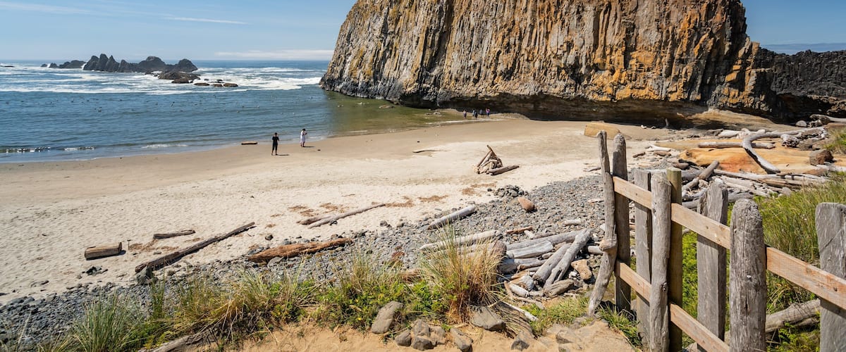 A rocky cliff by the sea, a sandy beach, and a wooden fence.