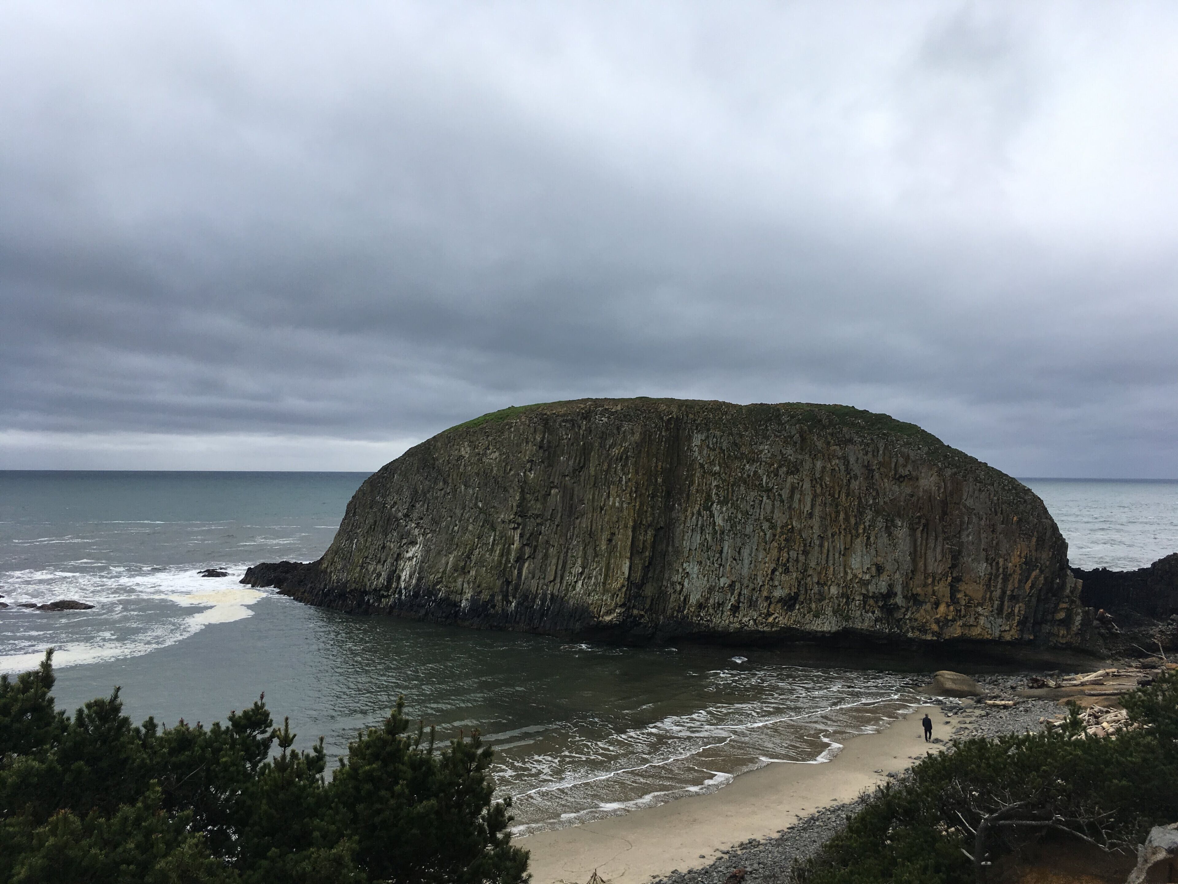 A large, rounded rock formation by the sea with a beach in the foreground.