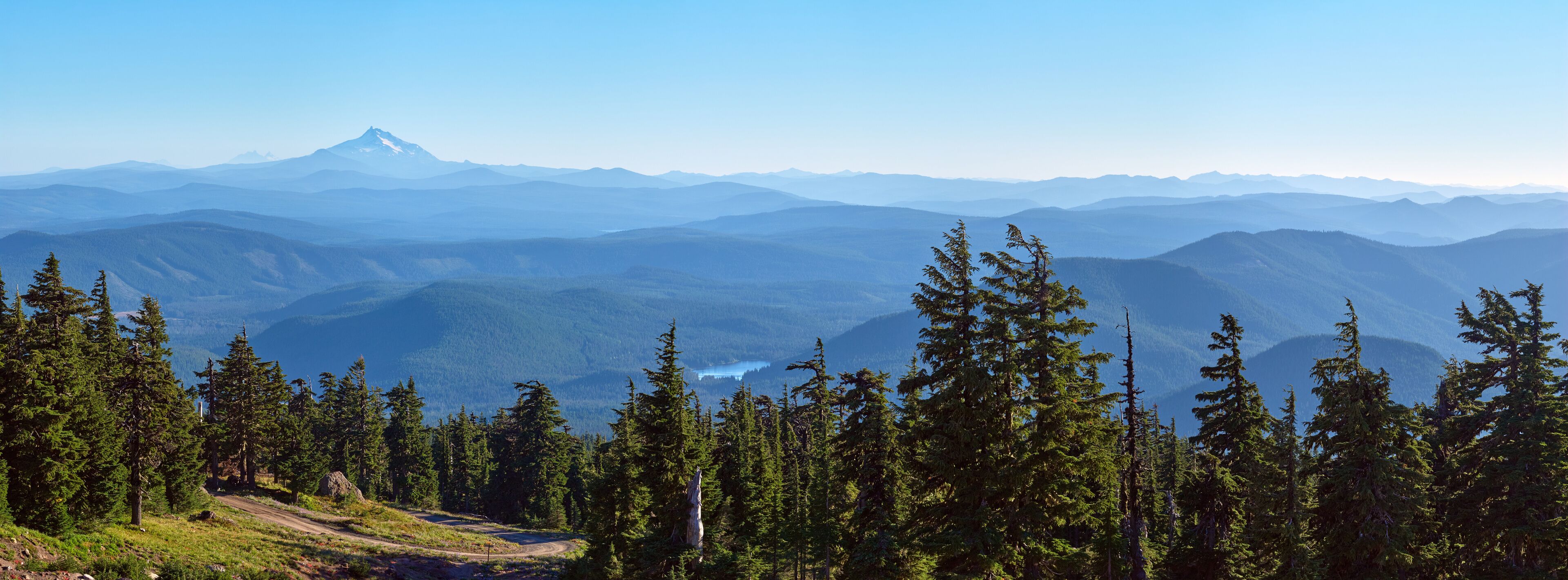 A mountain range with a prominent peak, dense forest, and a clear sky.
