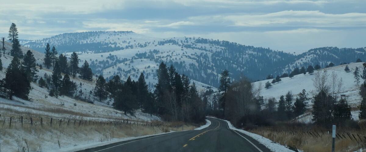 A snow-covered mountain road curving through a forested landscape.