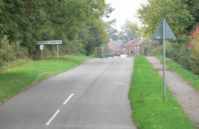 A rural road with a 'Church Langton' sign, a triangular warning sign, and a pedestrian path alongside.