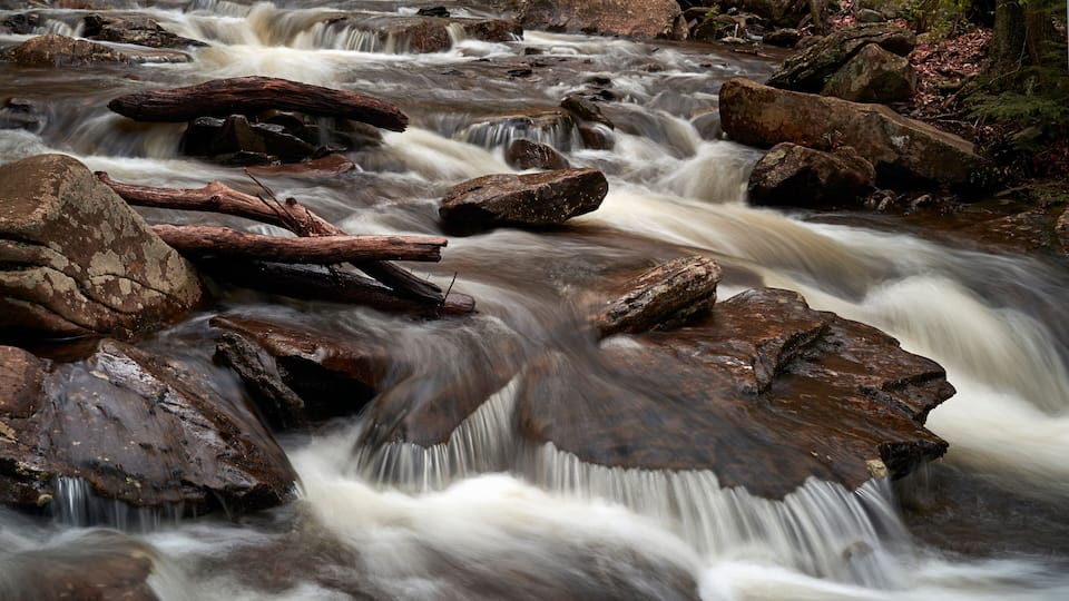 A fast-flowing river with large rocks and fallen logs.