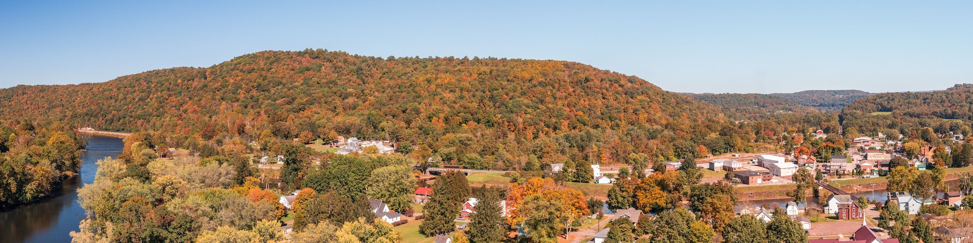 A river flowing through a town surrounded by autumn-colored trees and hills.