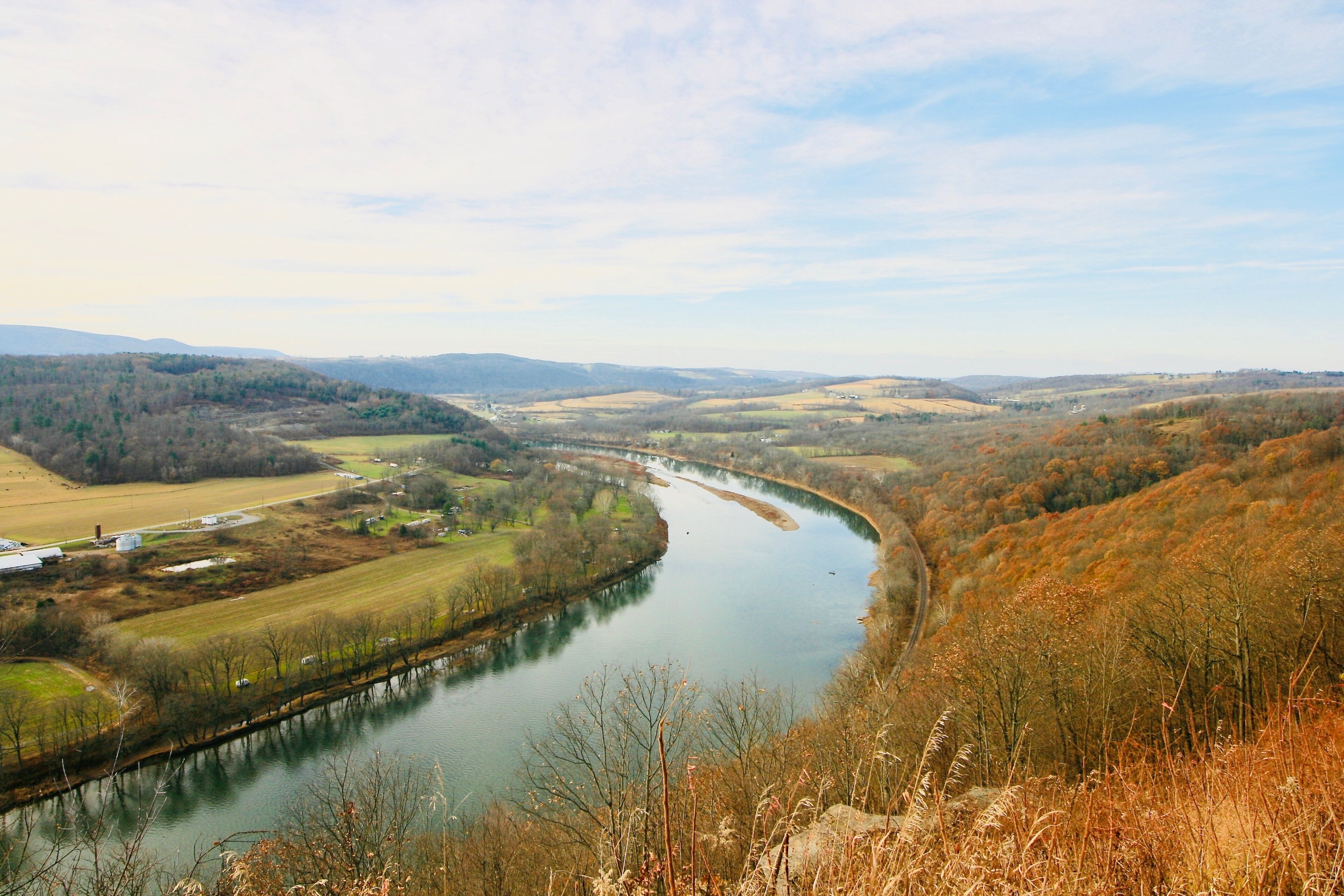 A river winding through a valley with fields and trees, surrounded by hills.